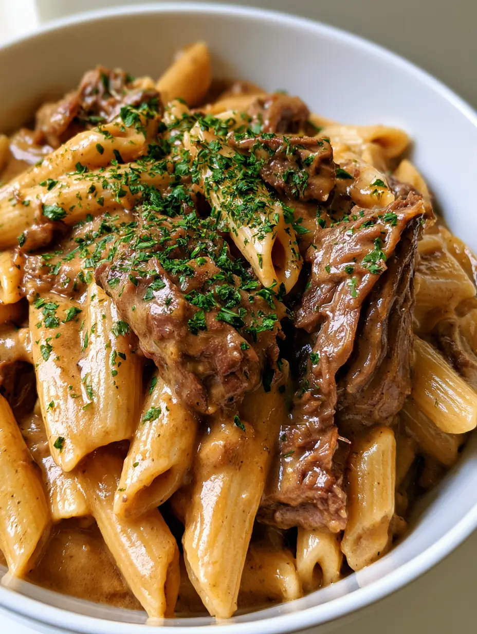 A close-up handheld smartphone photo of Slow Cooker Garlic Beef Pasta in a white ceramic bowl showing the glossy cream sauce.