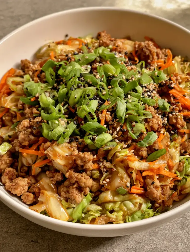 Egg Roll in a Bowl served on a neutral grey stone countertop in soft daylight, showing black and white sesame seed garnishes.